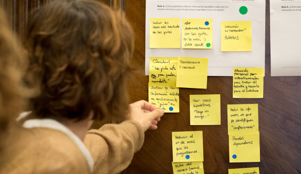 Una persona coloca un post it en una pared en la que hay otras tarjetas escritas con ideas